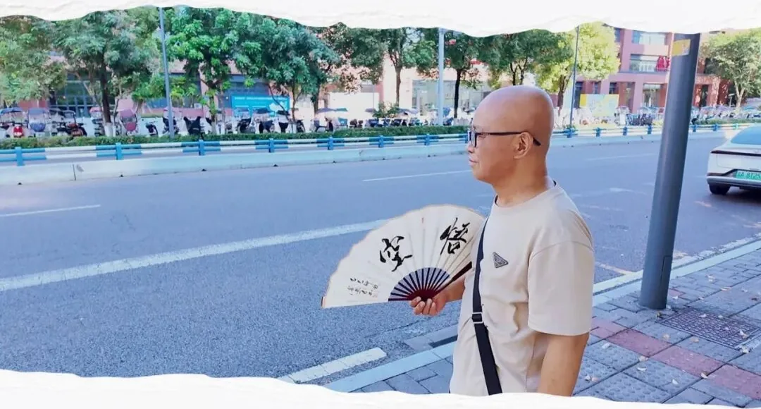 Mr. Shi holding a folding fan with calligraphy on a street in Chongqing